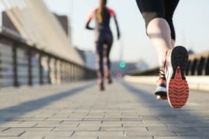 Two female runners running along a bridge. Biomechanical assessments by trained podiatrists can help you run better.